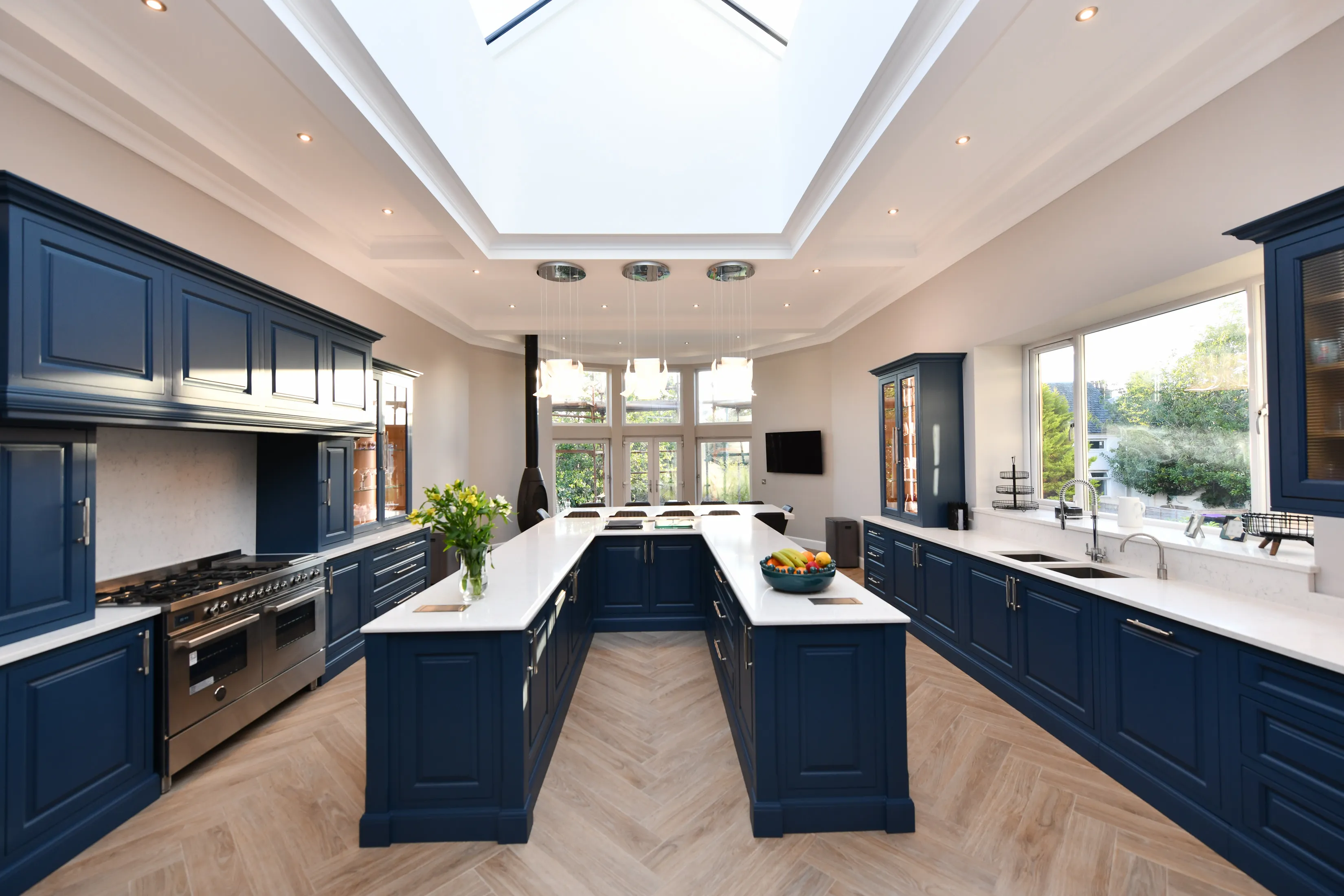 Large handmade kitchen featuring a large U shaped central island, lots of storage, lit glass cabinets and a pantry, viewed from the entrance