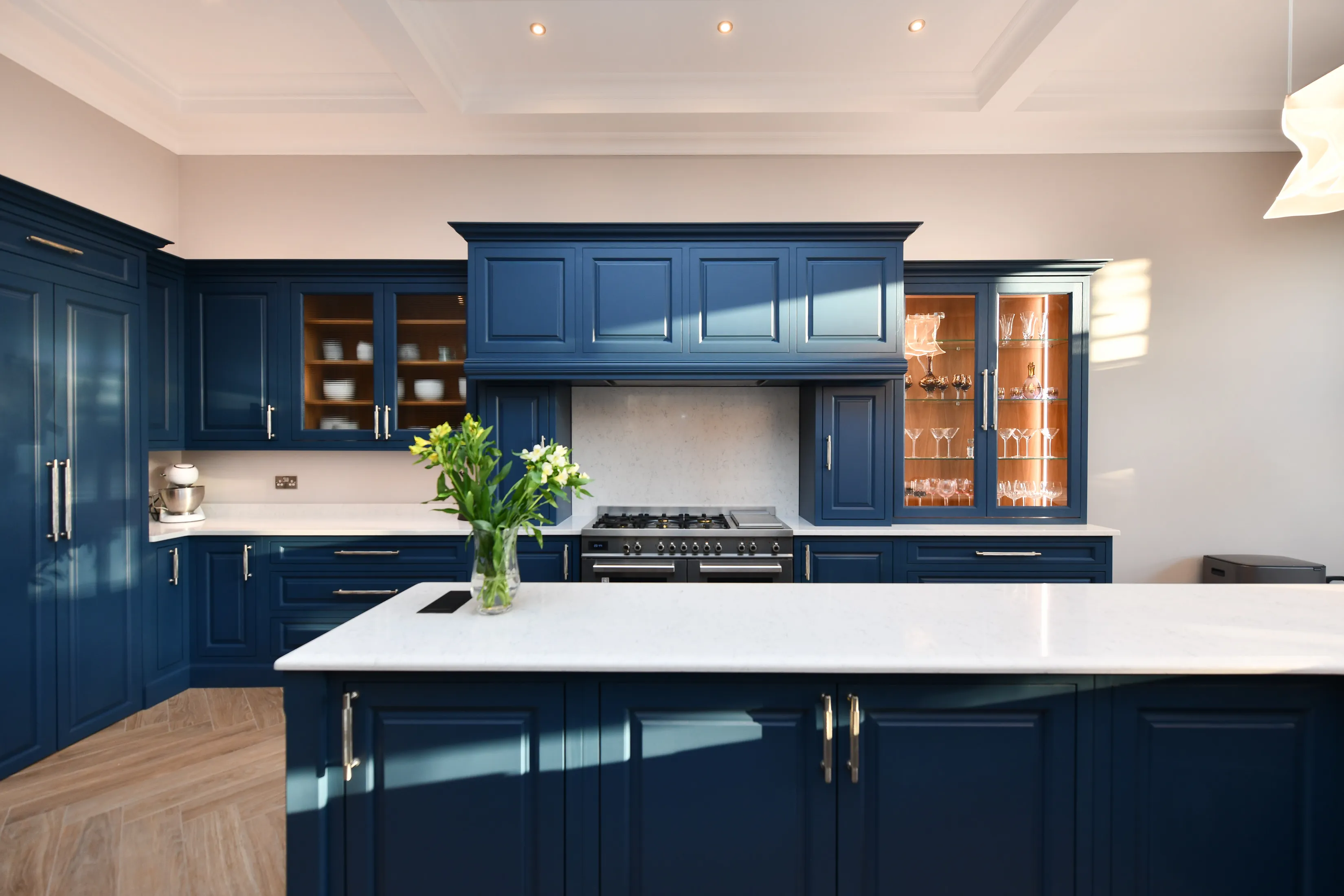 View across central island in large handcrafted kitchen featuring a double oven, large drawers and cupboard storage, some with display windows