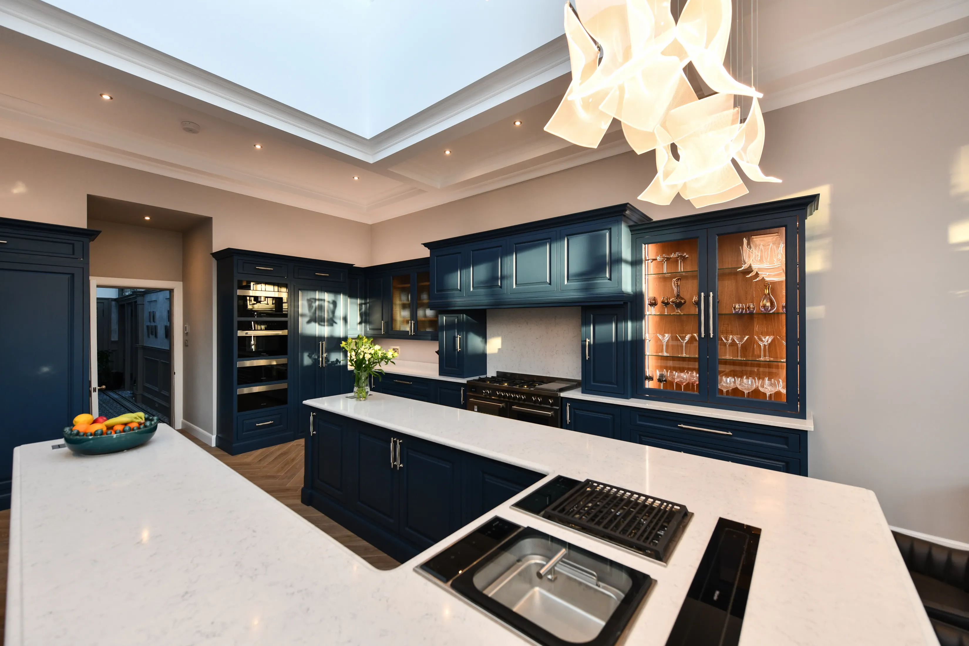 Large handmade kitchen featuring a large U shaped central island, lots of storage, lit glass cabinets and a pantry, iewed looking towards the range cooker